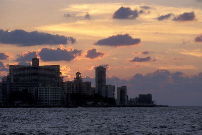 Sea by buildings against sky during sunset