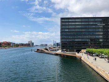 Modern buildings by river against sky in city