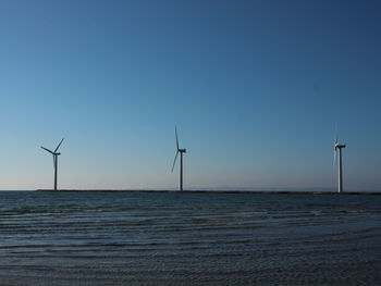 Wind turbines on sea against clear sky