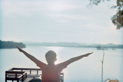 Rear view of man standing by lake against sky