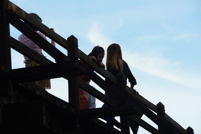 Low angle view of women standing on railing against sky