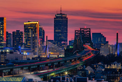 Illuminated modern buildings in city against sky at sunset