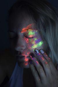 Woman with multi colored painted face against black background