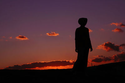 Silhouette woman standing on land against sky during sunset