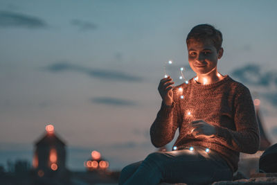 Full length of boy sitting against illuminated sky at dusk