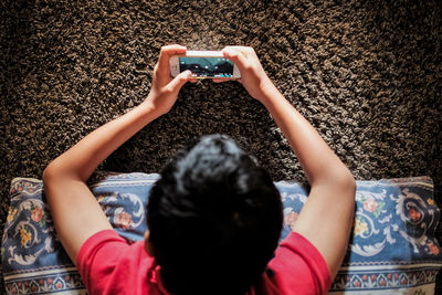 High angle view of boy playing video game in smart phone at home