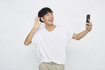 Full length of smiling man holding mobile phone against white background