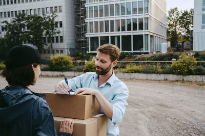 Mature man signing on documents while receiving packages from delivery person