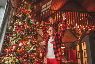 Candid authentic happy dad and son in red plaid pajamas fooling around at wood lodge xmas decorated