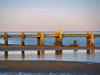 Wooden posts in sea against clear sky