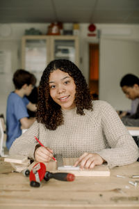 Portrait of female teenage student with ruler and pencil during carpentry class at high school