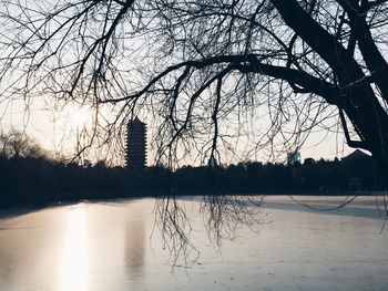 Reflection of bare trees in lake against sky