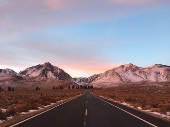 Empty road leading towards mountains against sky during winter