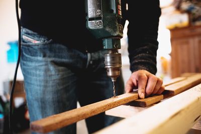 Midsection of man drilling wood at workshop