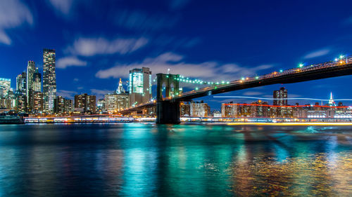 Illuminated brooklyn bridge over east river against sky at night