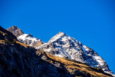 Low angle view of snowcapped mountains against clear blue sky