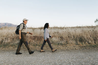 Full body side view of mature couple in casual clothes walking on grassy meadow in countryside