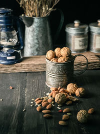 Walnut in a tin mug and other variety of nut on a dark table with iron containers and jug