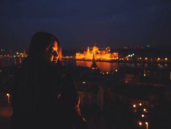 Woman standing by illuminated cityscape against sky at night