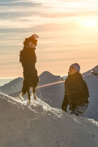 People on snow covered land against sky during sunset