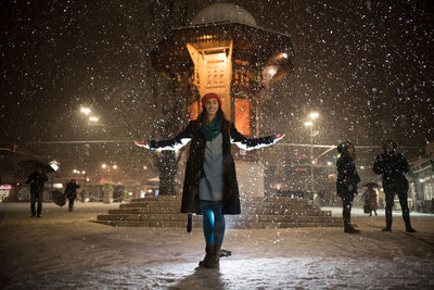 Full length of woman with umbrella in illuminated city at night