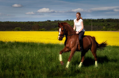 Full length of young woman riding horse on field