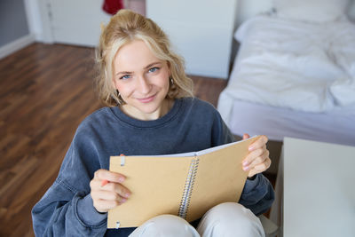 Portrait of young woman reading book at home