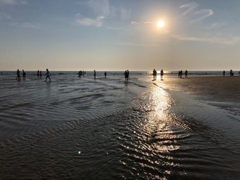 People at beach against sky during sunset