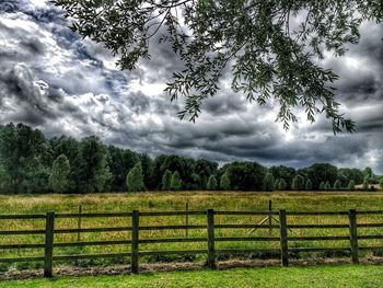 Fence on grassy field against cloudy sky