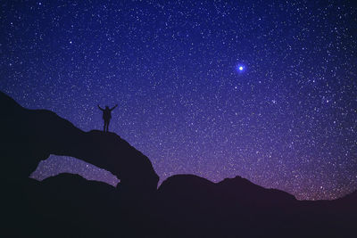 Low angle view of silhouette person standing on rock formation against star field in sky at night
