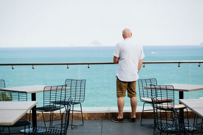 Rear view of man standing on terrace restaurant by sea