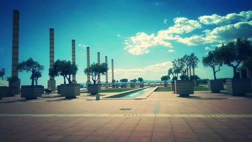 Palm trees by swimming pool in city against sky