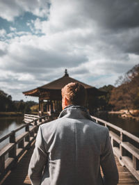 Rear view of man standing by railing against sky