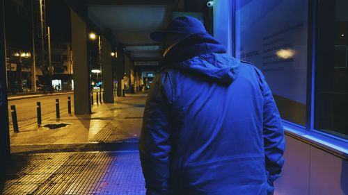 Rear view of man in warm clothing walking on sidewalk at dusk