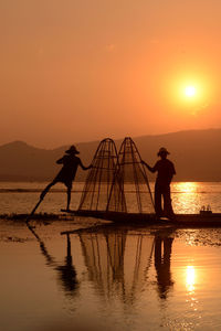 Silhouette men fishing in lake at sunset