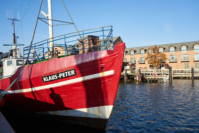 Red ship moored in sea against sky in city