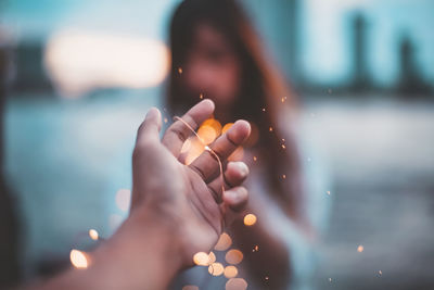 Cropped hand against defocused lights and woman 