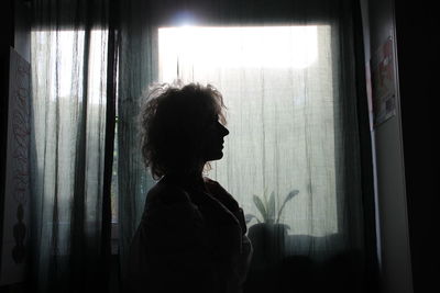 Portrait of woman looking through window at home