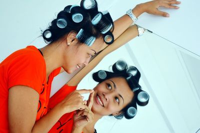 Tilt shot of woman with hair curlers touching reflection in mirror on wall