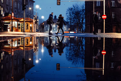 People reflecting in puddle on street at night during monsoon