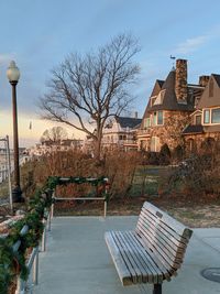 Empty bench by street and beach houses against sky