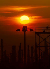 Silhouette street lights against orange sky during sunset