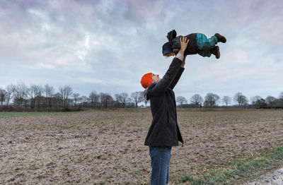 Cheerful father holding daughter against sky while standing on field 