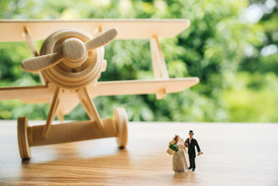 Close-up of toy airplane with figurines on wooden table against trees