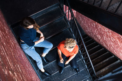 High angle view of female friends talking while sitting together on steps at home
