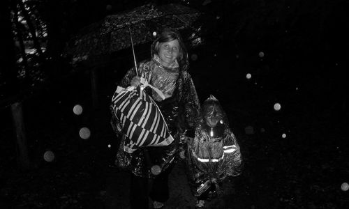 Young woman with umbrella and son walking through the rain at night