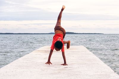 Full length of boy doing handstand at beach against sky