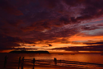 Silhouette people on beach against sky during sunset