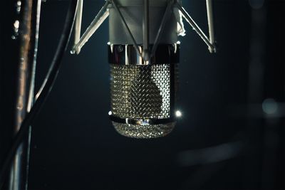 Close-up of illuminated lighting equipment hanging against black background