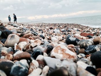 People walking on rocks at beach against sky